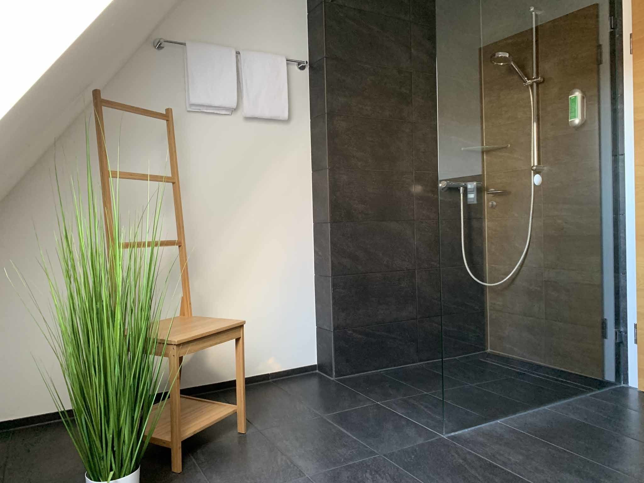 Un baño moderno con cabina de ducha de vidrio, una silla de madera y una planta en maceta.