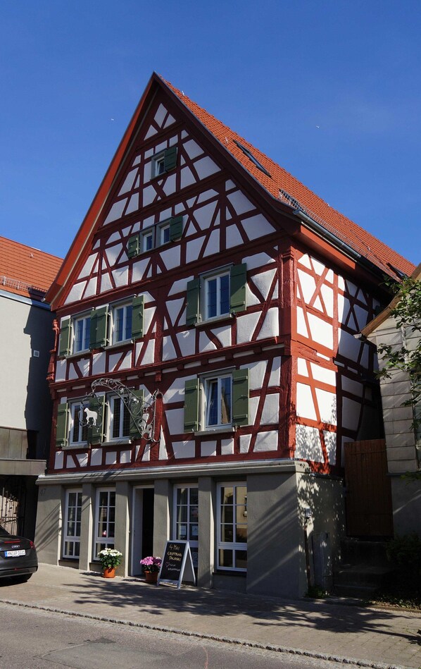 A traditional half-timbered building with multiple windows and a signboard in front. - Pension Pauserei (Oedheim)