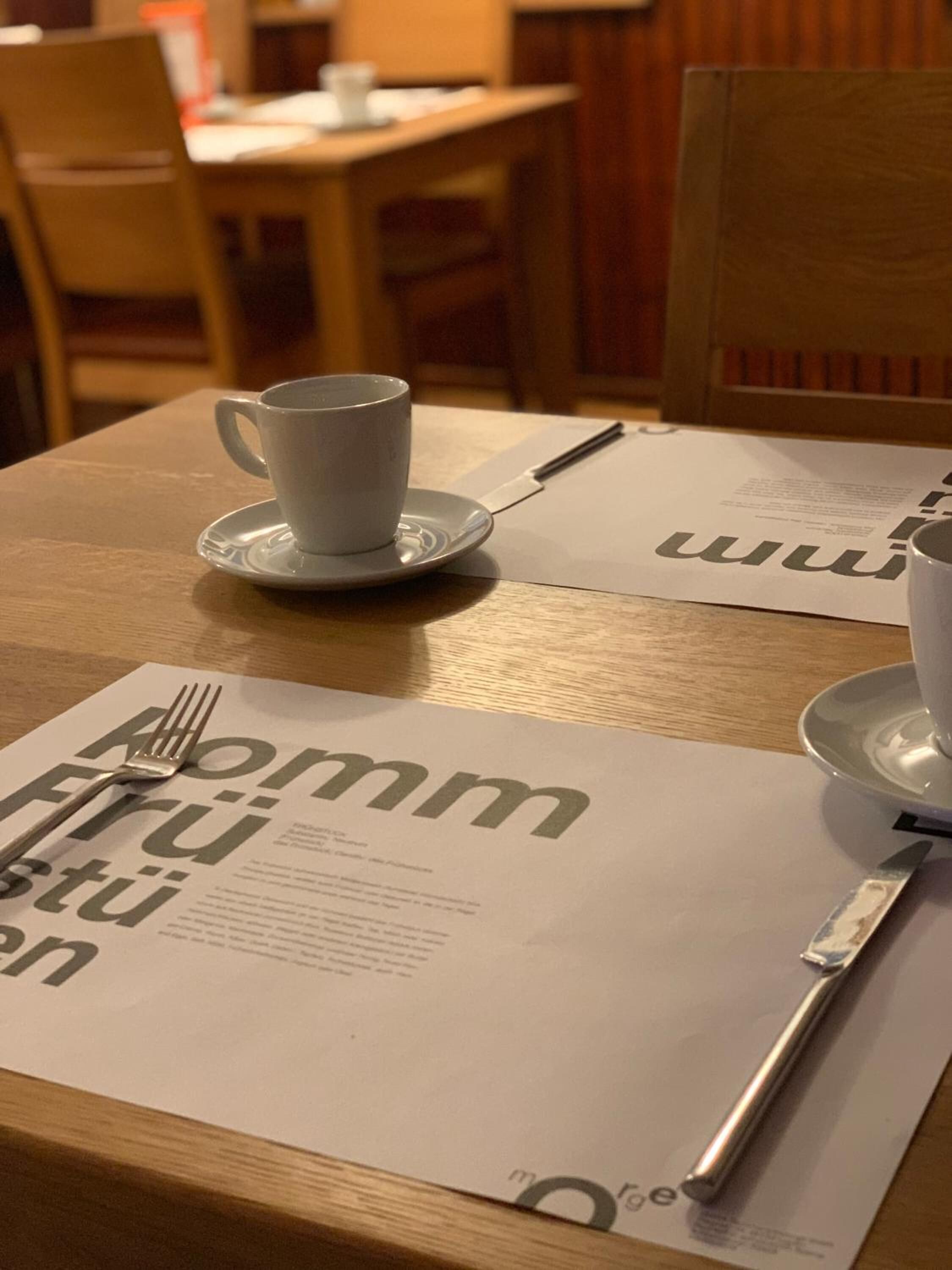 Une table avec une tasse et une soucoupe blanches, une fourchette et un menu.