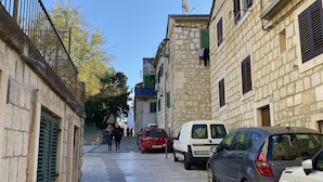 A narrow street with stone buildings, parked cars, and a clear blue sky. - Studio Apt Orchard on Rokova St (Split)