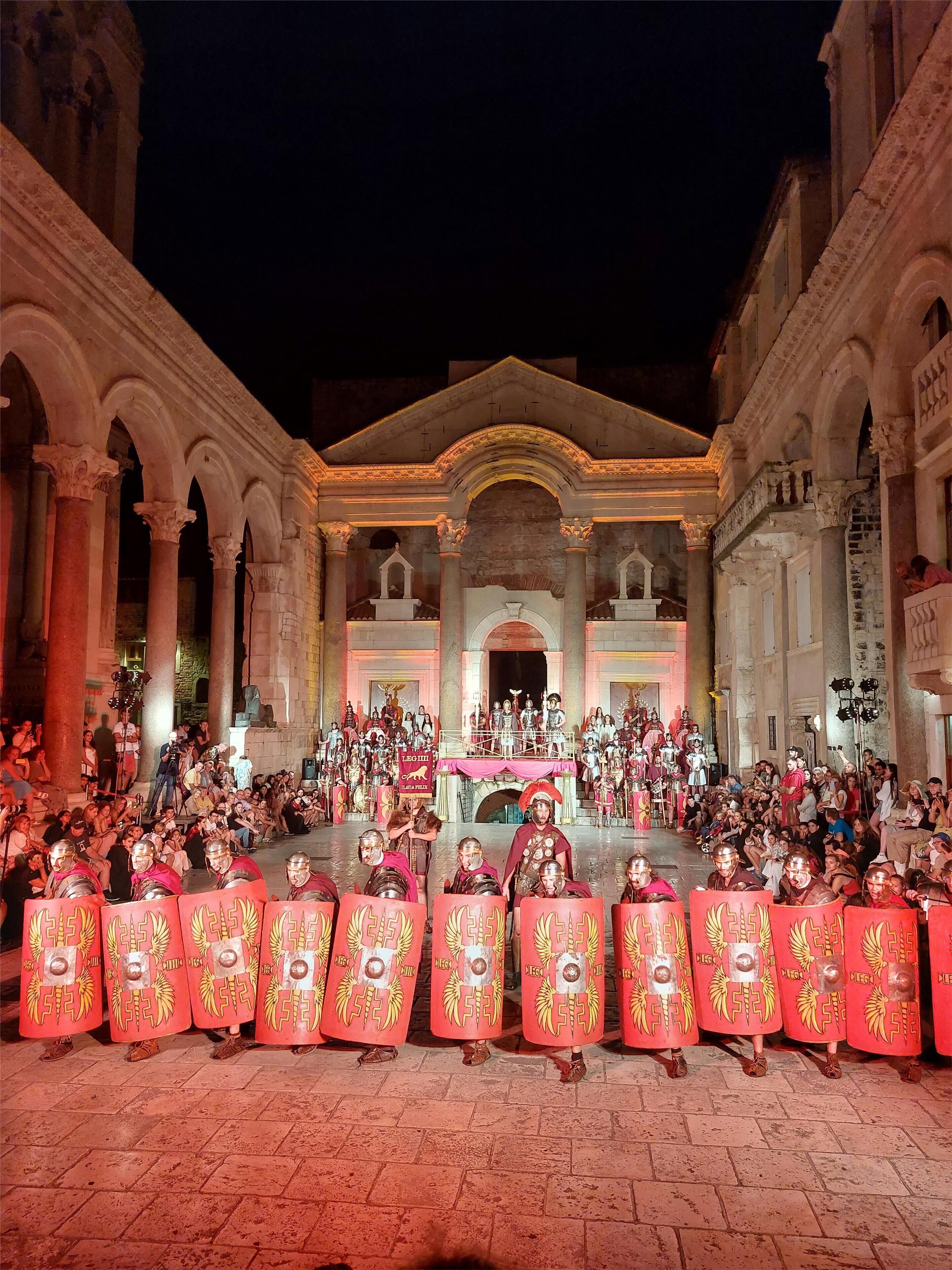 A historical building with classical architecture, including columns and arches, hosting a public event with people in period costumes.