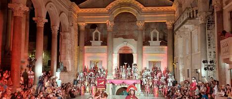 A historical building with classical architecture, including columns and arches, hosting a public event with people in period costumes.