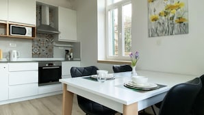 A modern kitchen with white cabinets, a microwave, and a coffee maker. There is a dining table with chairs and a vase with flowers. - Studio Apt Orchard on Rokova St (Split)
