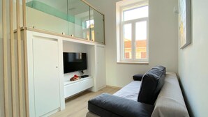 A modern room with a built-in TV, a glass partition, a window with a view, and a sofa. - Studio Apt Orchard on Rokova St (Split)