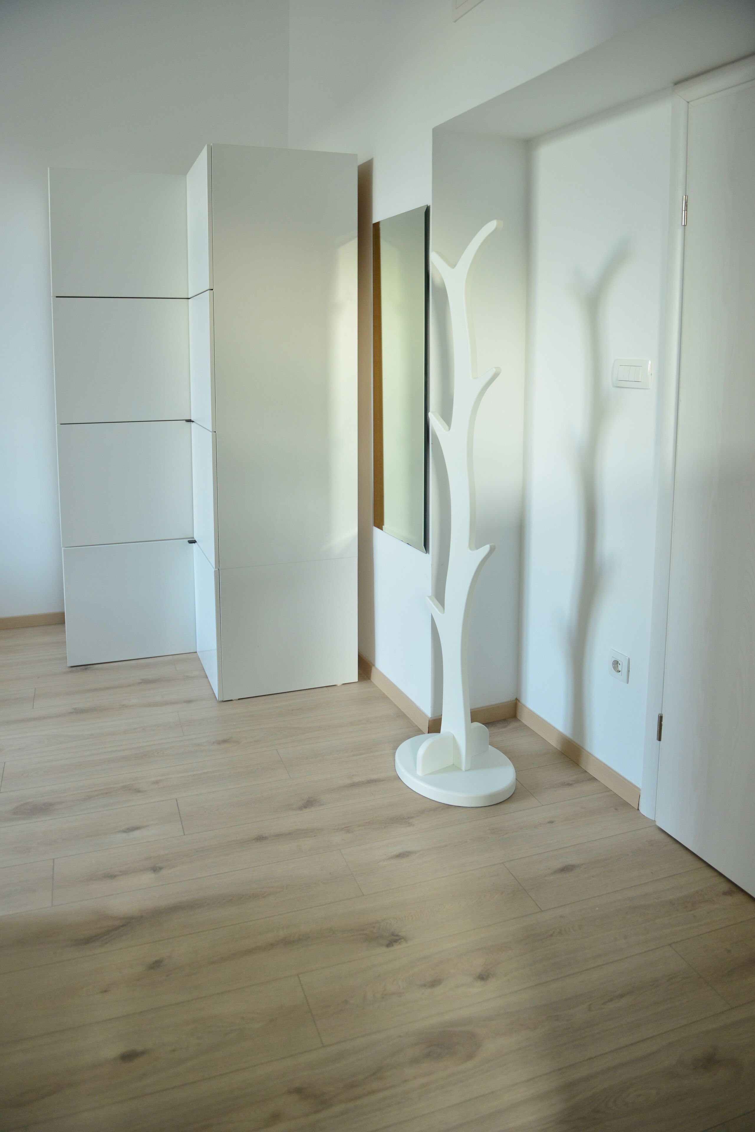 A room with a wooden floor, a white wardrobe, and a white abstract sculpture.