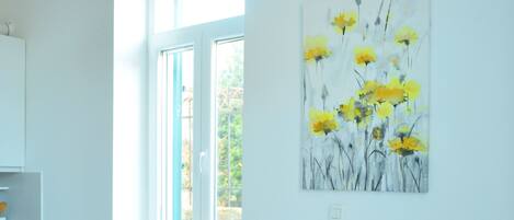 A dining area with a white table set for two, a vase with flowers, and a painting of yellow flowers on the wall.