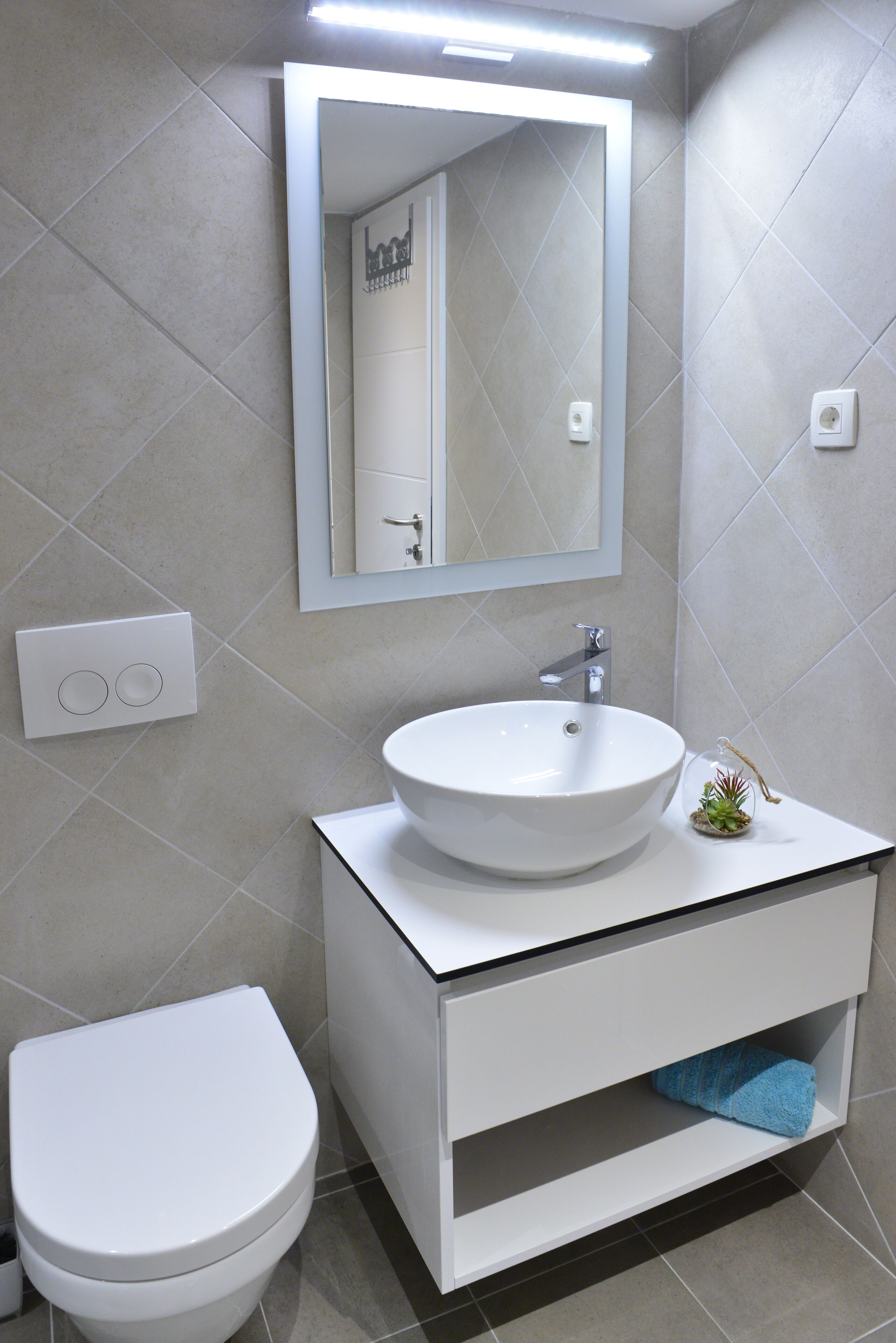 A modern bathroom with a white sink, a toilet, and a mirror above the sink.