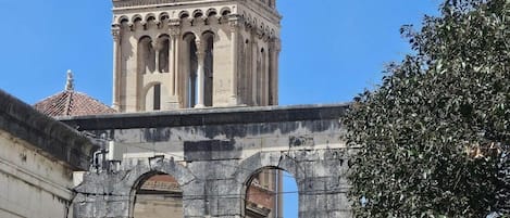 Una torre histórica con una cruz en la cima, rodeada de muros y arcos de piedra.