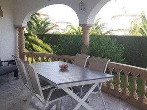 A covered patio with a table and chairs, a view of greenery, and a balustrade.
