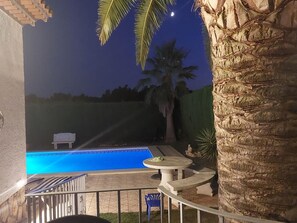 A swimming pool with a patio area, palm trees, and a night sky.