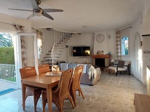 A spacious living area with a dining table, chairs, a sofa, a TV, and a staircase.