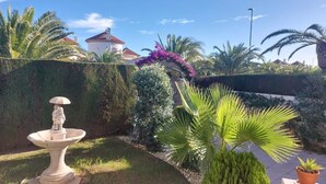 Ein gepflegter Garten mit Brunnen, Palmen und einer Hecke.