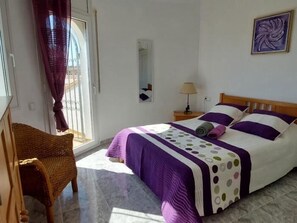 A bedroom with a bed, a chair, a nightstand, a lamp, and a window with curtains.