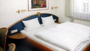 Une chambre d’hôtel avec un lit simple, une chaise, une table de chevet et un tableau au mur.