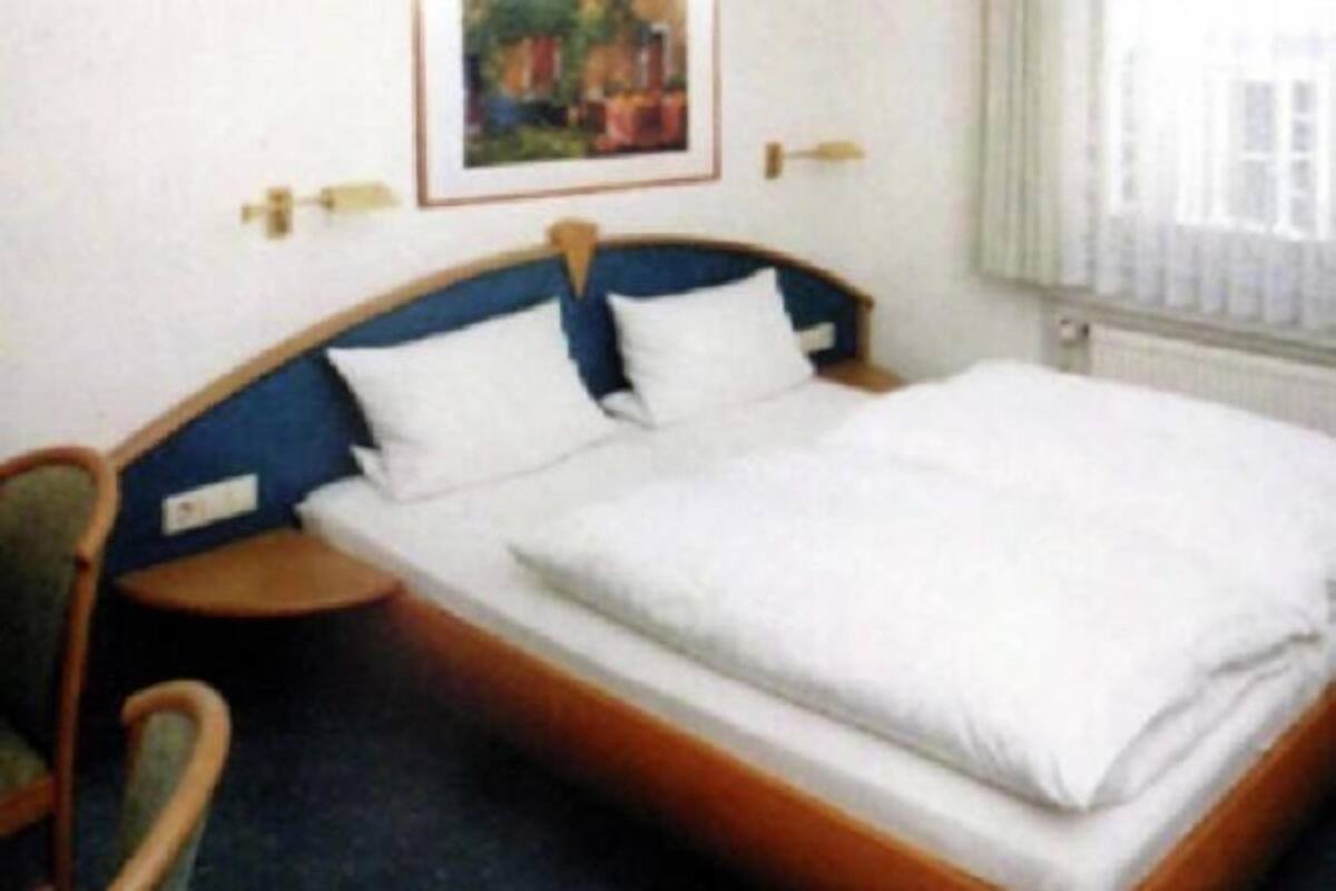 Una habitación de hotel con una cama individual, una silla, una mesita de noche y un cuadro en la pared.