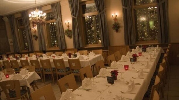 Une salle de banquet avec de nombreuses tables dressées pour le repas, de grandes fenêtres ornées de rideaux et un lustre.