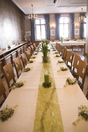Ein langer Bankettisch für eine festliche Veranstaltung, mit Stühlen an beiden Seiten und einer zentralen Blumenkomposition.