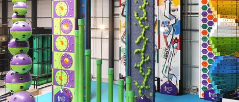A colorful indoor play area with various climbing structures and a large LEGO wall.