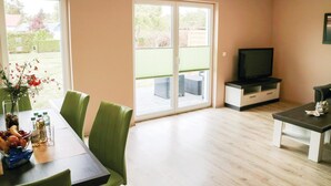 Un salon comprenant une table à manger, des chaises vertes, un meuble pour la télévision et une porte-fenêtre coulissante donnant sur un patio.