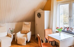 A cozy room with a sloped ceiling, a white chair, a table, and a window with a view of trees.