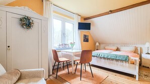 A bedroom with a bed, a desk, two chairs, a wardrobe, and a window with curtains.