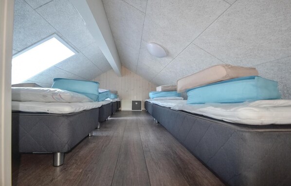 A narrow, tiled room with multiple beds aligned against the walls, a skylight, and a wooden floor.