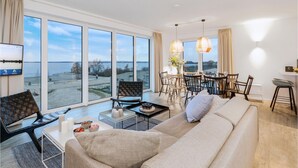 A spacious living room with a large sofa, a dining area with a table and chairs, and a view of the beach through large windows. - Luxurious apartment in Lembruch/Dümmer See with house sea view (Lembruch/Dümmer See)