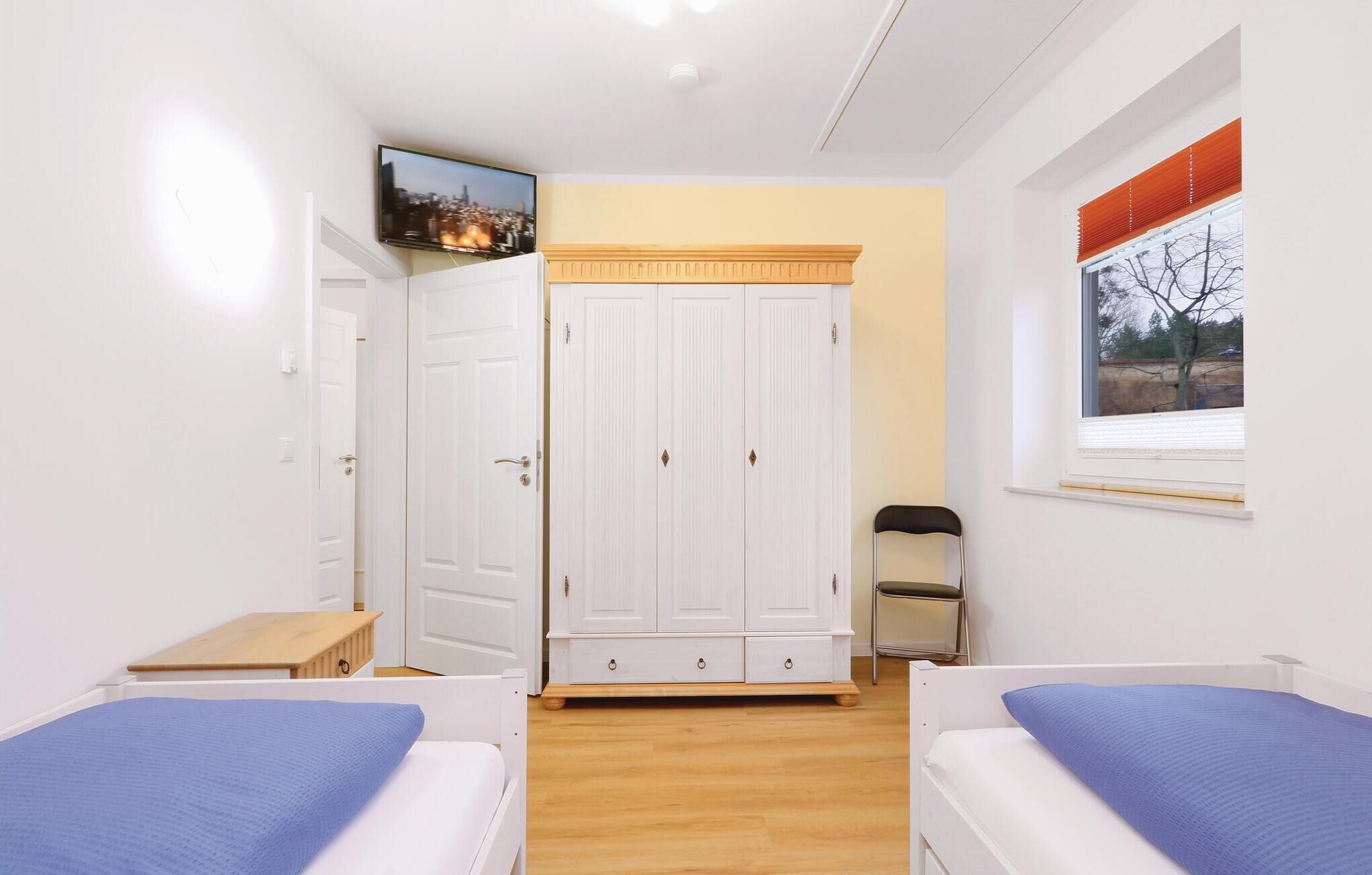 A bedroom with two beds, a wardrobe, a television, and a window with blinds.