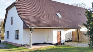 Une maison à deux étages avec un toit recouvert de tuiles brunes, un petit garage attenant et une porte d’entrée.
