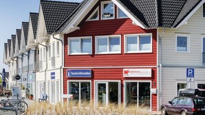 Une rangée de bâtiments modernes à la façade rouge et blanche, un panneau indiquant un bureau d’information touristique et un panneau indiquant un bureau de services Novasol.