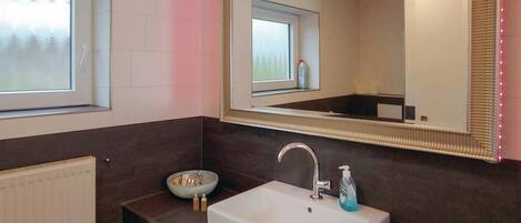A bathroom with a white sink, a mirror, and a window.