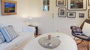Un salon avec un canapé blanc, une table basse ronde sur laquelle repose un vase décoratif, une lampe et des œuvres d’art encadrées accrochées au mur.