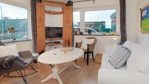 Un salon chaleureux avec un canapé blanc, une table ronde et un téléviseur fixé au mur, qui est en bois.