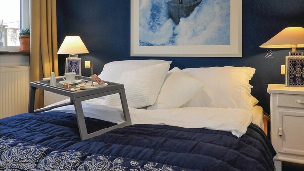 Une chambre d’hôtel avec un lit, deux tables de chevet, une lampe, un tableau encadré au mur et une fenêtre avec des rideaux.
