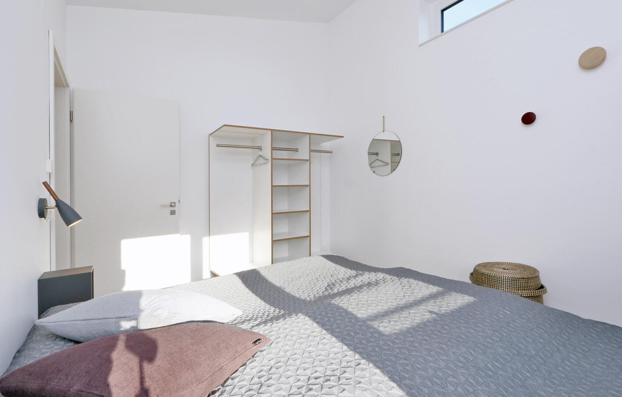 Une chambre à coucher comprenant un lit, une armoire, une lampe suspendue, un miroir et un petit panier en osier.