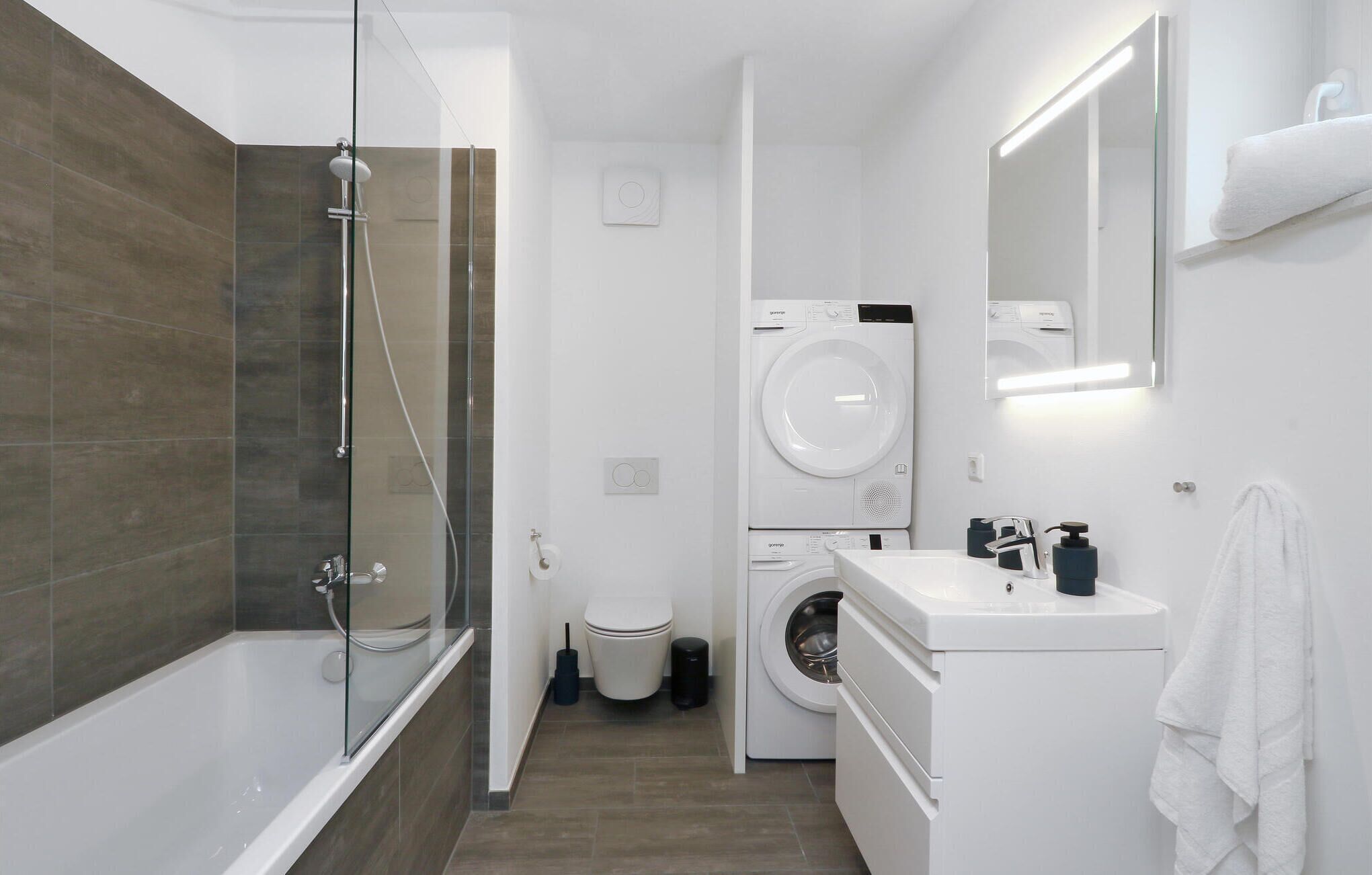 A modern bathroom with a glass-enclosed shower, a washing machine, and a sink with a mirror above.
