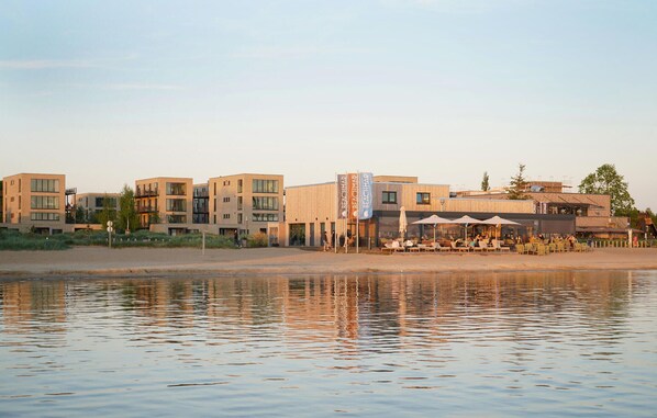 A waterfront hotel with modern architecture, outdoor seating, and a beach view.