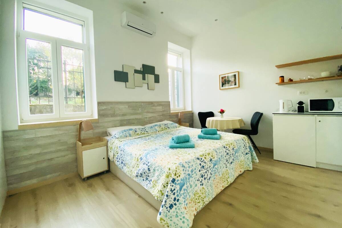 A bedroom with a bed, a desk, a chair, and a kitchenette.