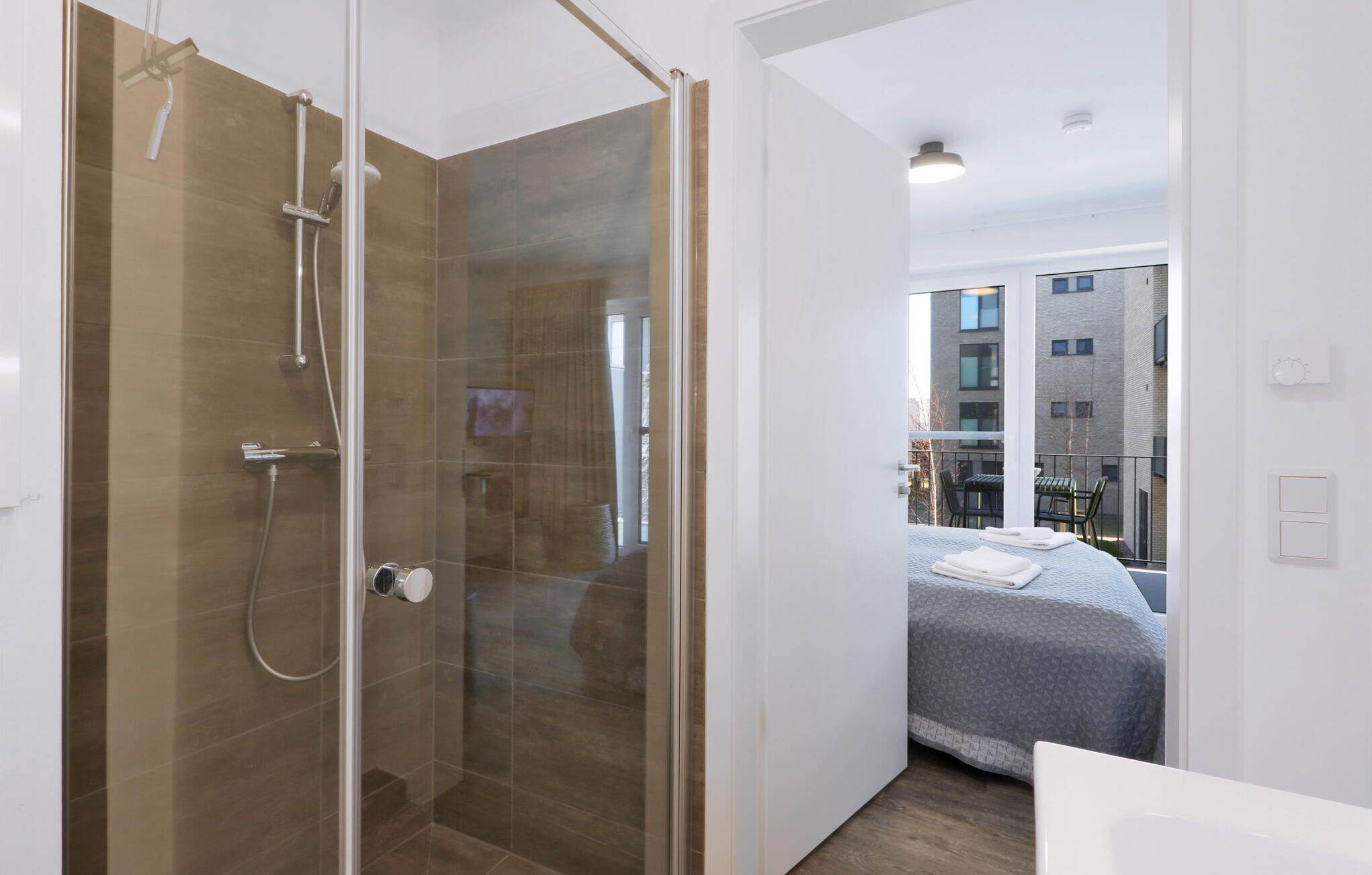 Un baño moderno con cabina de ducha de vidrio, un inodoro a la vista y una cama con vistas a la ciudad.