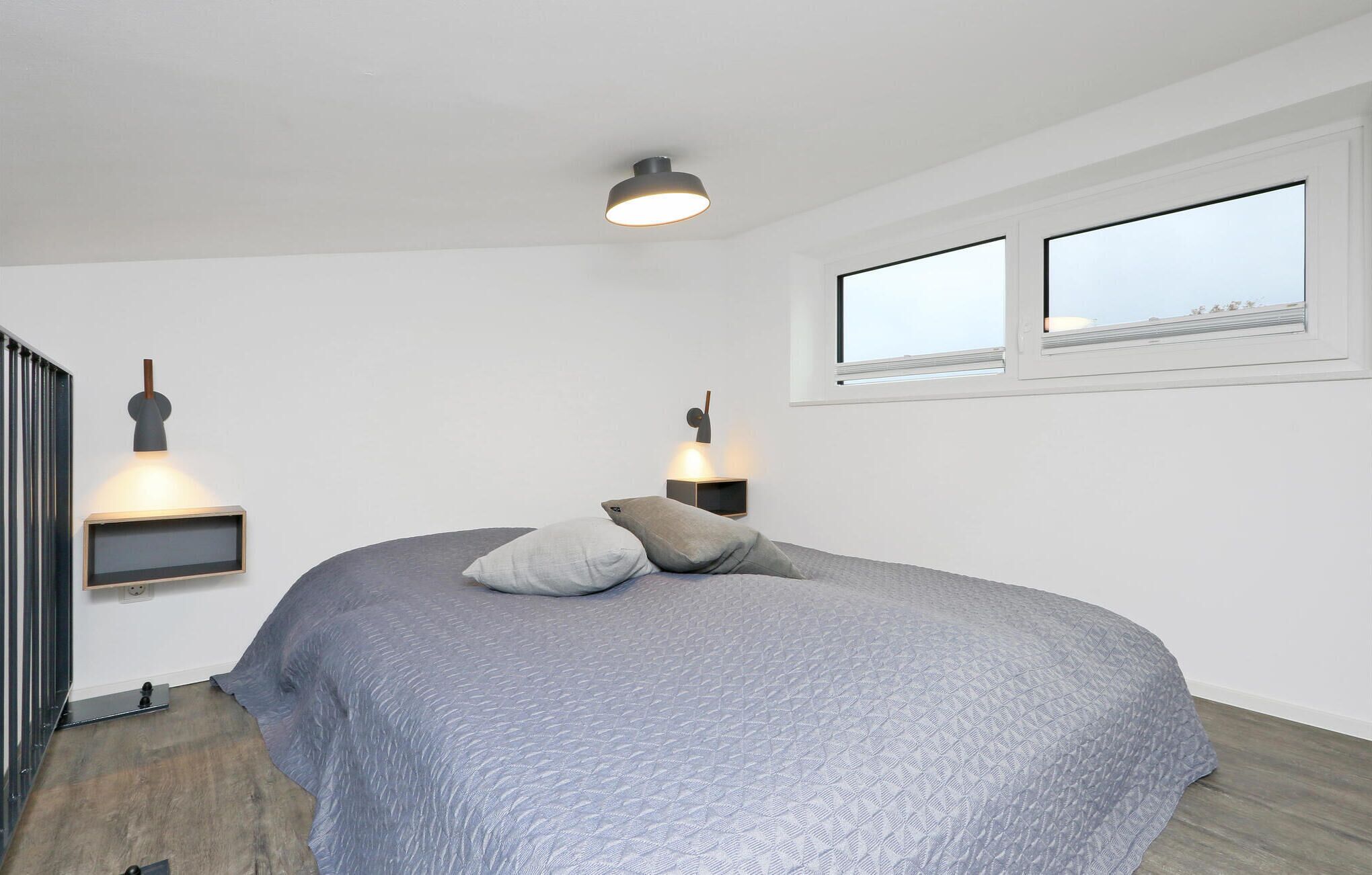 Un dormitorio con una cama, dos lámparas fijadas a la pared, una ventana y una puerta.