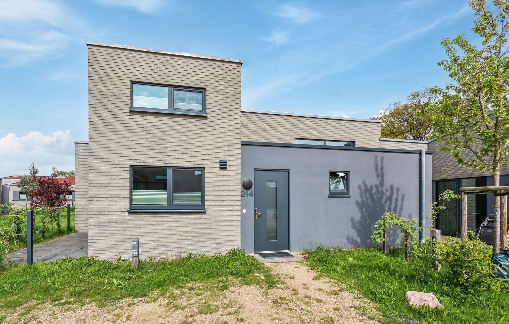 A modern two-story house with a flat roof, a small porch, and a well-maintained garden.