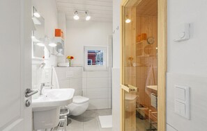 Een moderne badkamer met een wit wastafel, toilet en douchegedeelte. Er is een raam met uitzicht en een spiegel boven de wastafel.
