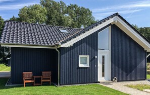 Een donker gebouw met een schuin dak, een groot raam en twee houten stoelen ervoor.