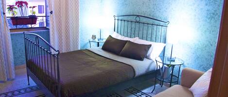 A bedroom with a metal bed frame, a bedside table with a lamp, a small round table, and a chair.