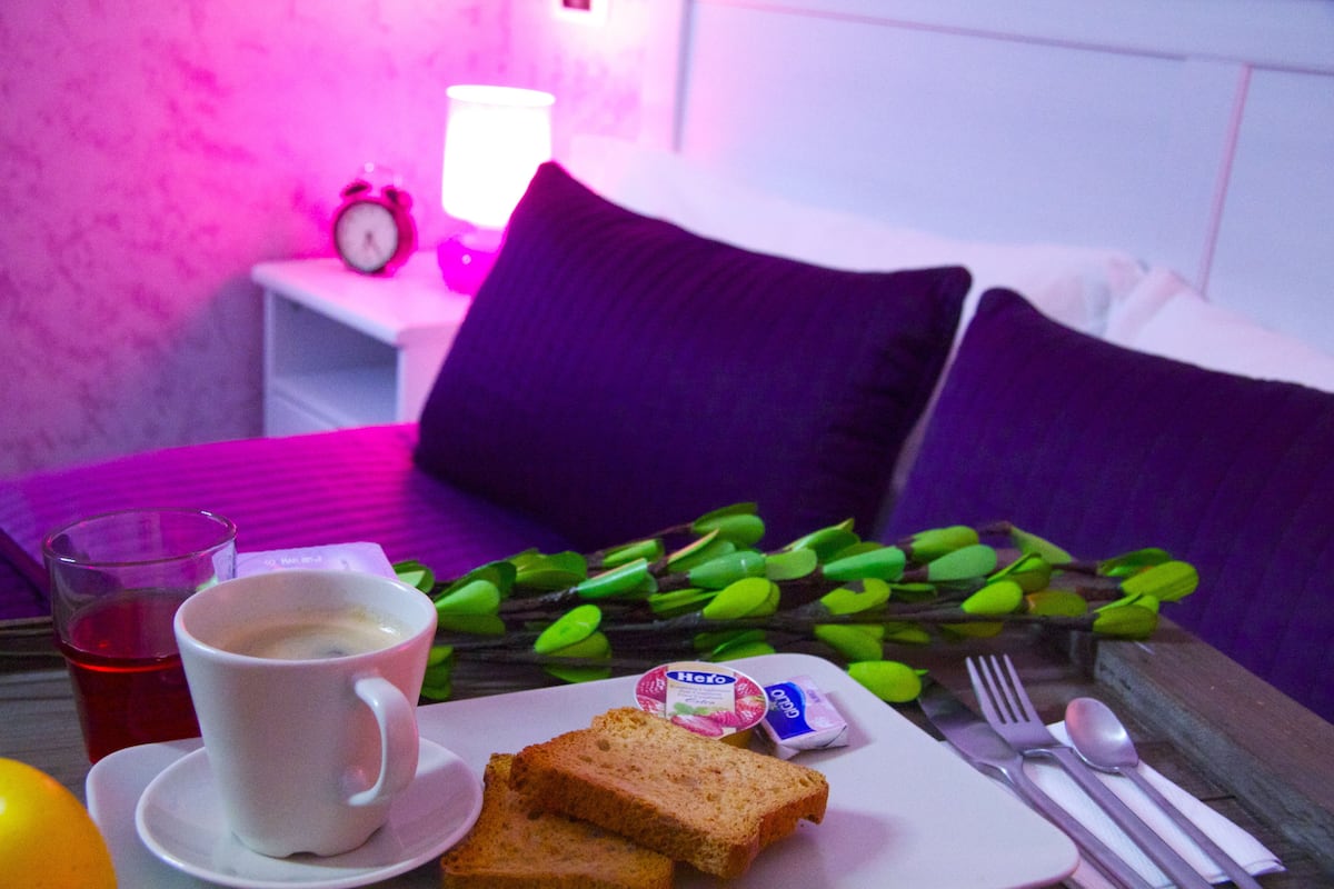 A breakfast setup with a cup of coffee, toast, butter, and jam on a tray, with a bed and pillows in the background.