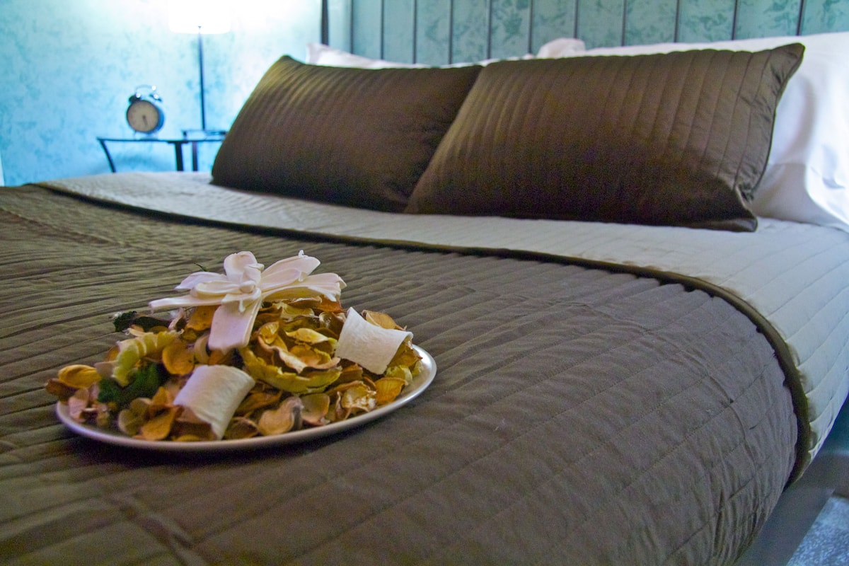 A neatly made bed with a brown quilt, a plate of food on the bed, and a clock on a bedside table.