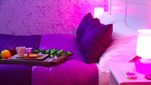 Habitación con decoración púrpura, que incluye una cama, una mesita de noche y una bandeja con comida y bebidas.
