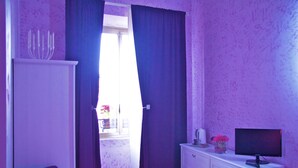 Una habitación con paredes moradas, un armario blanco, un televisor en una cómoda y una ventana con cortinas.