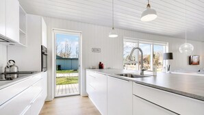 A modern kitchen with white cabinetry, a stainless steel kettle, a sink, and a large window. - Nice home in Glesborg with sauna (Glesborg)