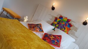 A bed with a yellow blanket, two colorful pillows, and a white headboard. - Asinerie Kuleni (Ponteilla)